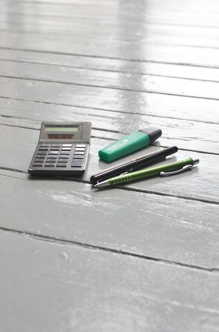 A calculator and pens on a wooden desk, ideal for business or study themes.
